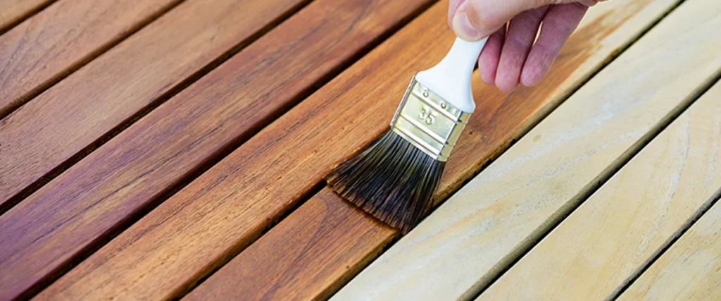 hand holding a brush applying varnish paint on a wooden garden table