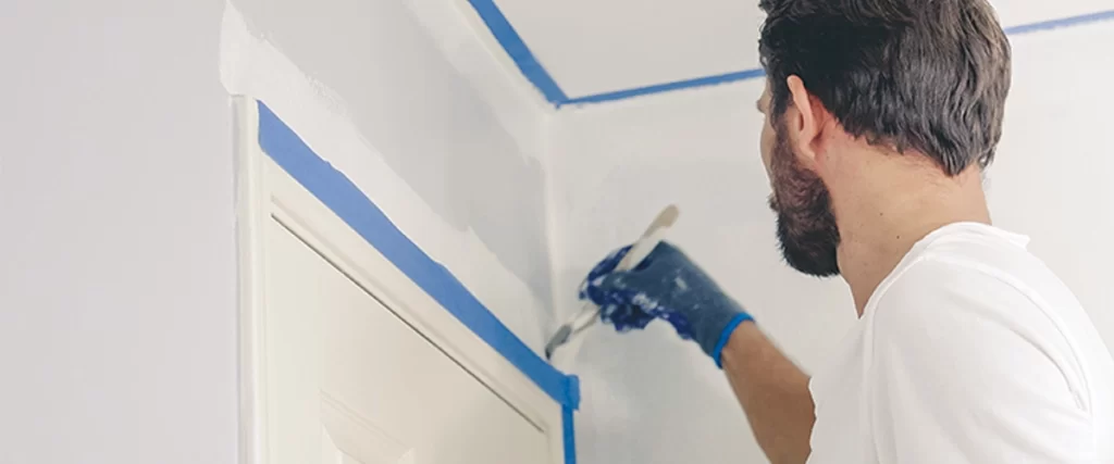 Close up of painter hands with gloves painting the wall edge by door frame