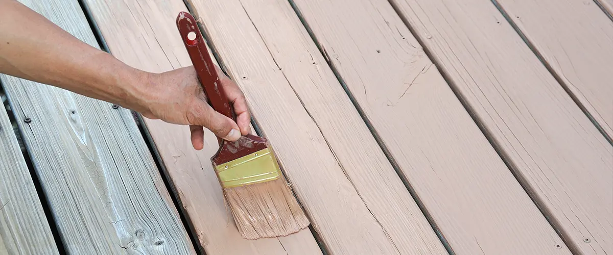 Close-up of a hand painting a wooden deck with a brown stain for a fresh, updated outdoor look.