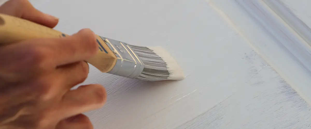 Close-up of hand painting a cabinet door with white paint. Cabinet refinishing and home improvement concept.