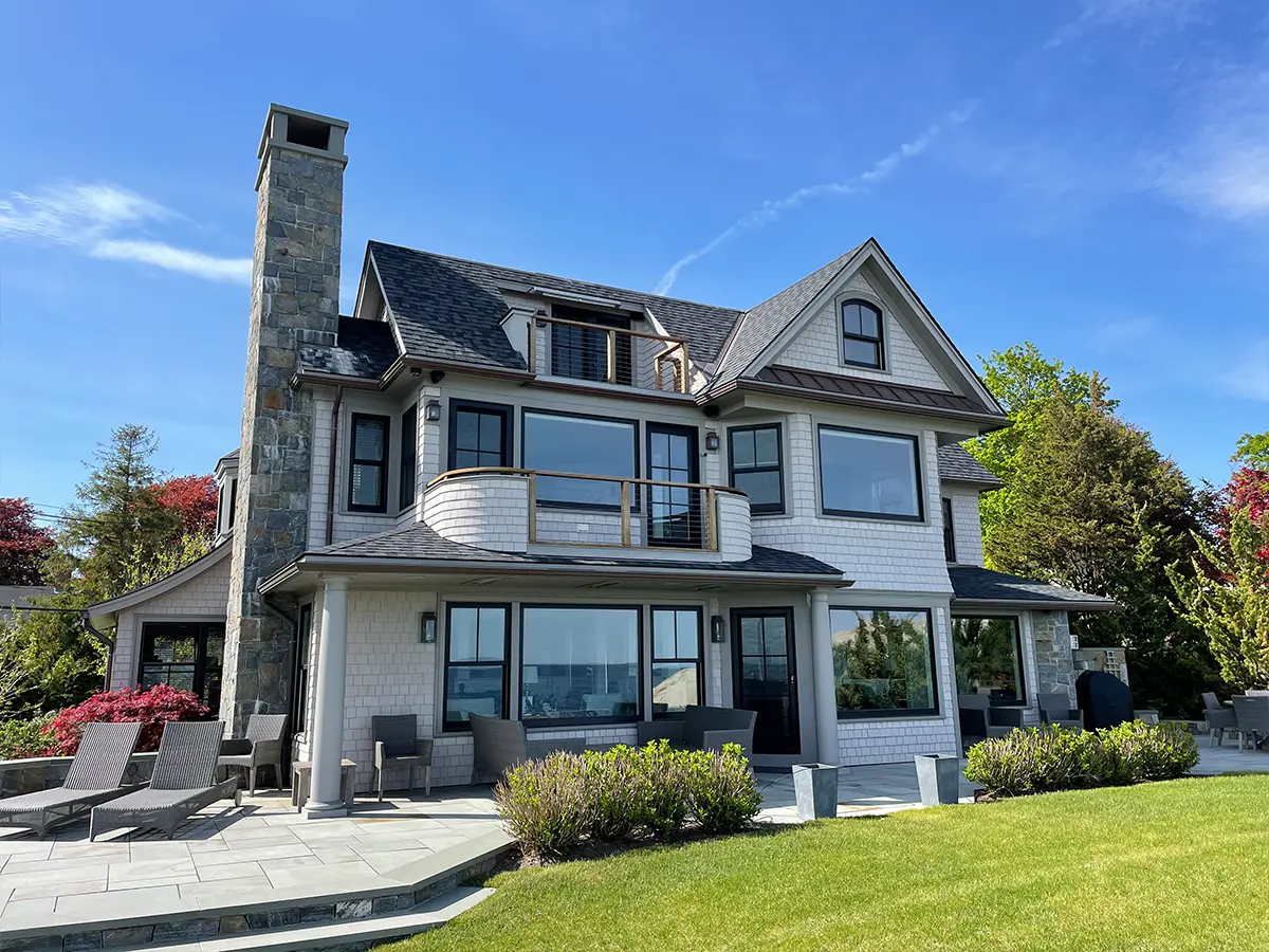 Luxury lakefront home with stone chimney and gray siding.