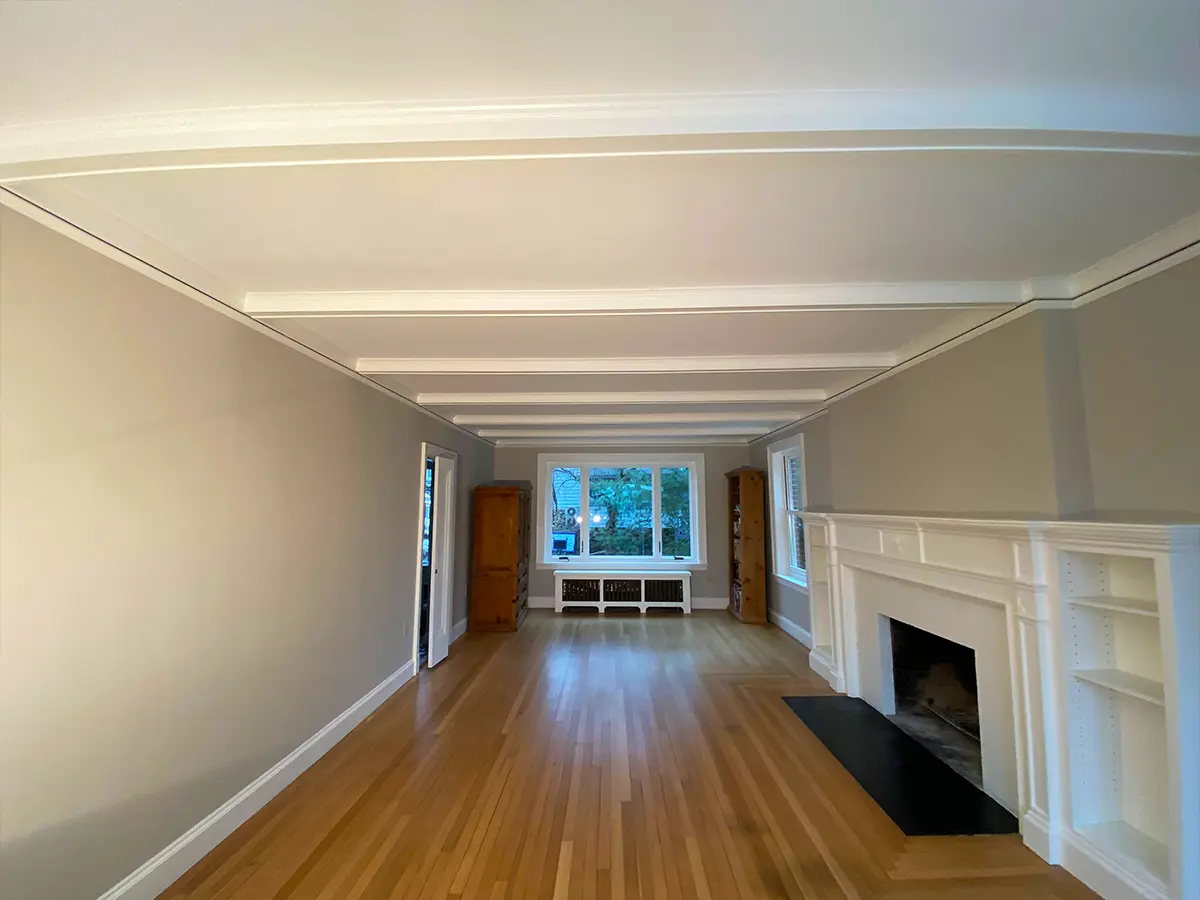 Restored living room with white beams, fireplace, and hardwood flooring, offering a clean, bright aesthetic.