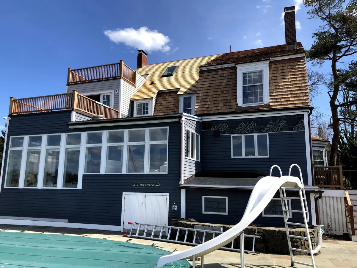 Blue house with large windows and outdoor pool area, featuring a slide and sundeck.