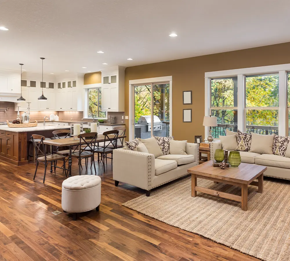 Warm open-concept living room and kitchen with beige sofas, wood table, and large windows.