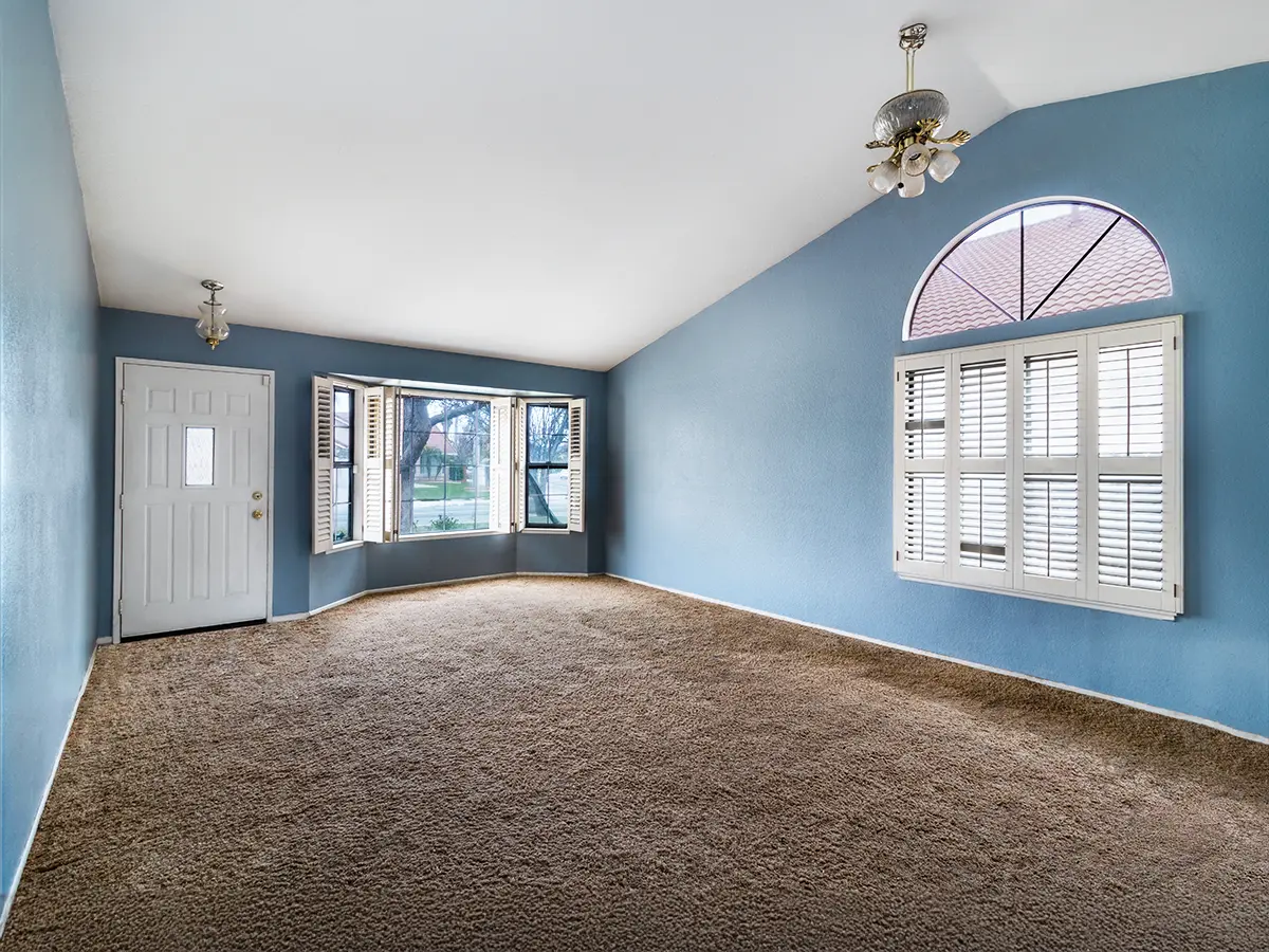 Spacious living room with blue walls and large arched window with plantation shutters