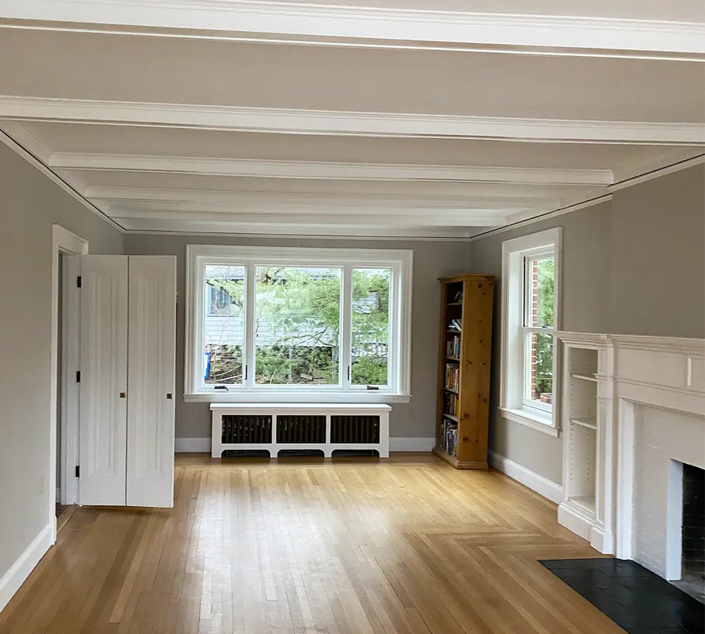 Renovated living room with white ceiling beams and hardwood floors, emphasizing natural light and space.