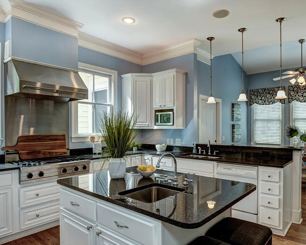 Modern kitchen with white cabinetry, black granite countertops, and stainless steel range, illuminated by pendant lights.