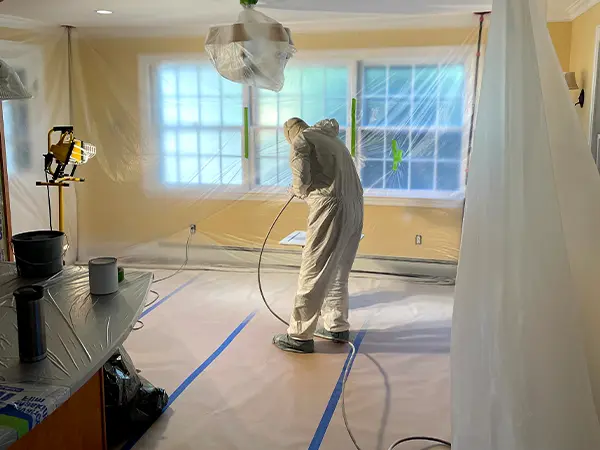 Professional painter in protective gear preparing a room for spray painting