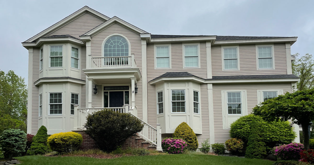 Elegant beige two-story home with manicured front lawn, bay windows, and professional landscaping