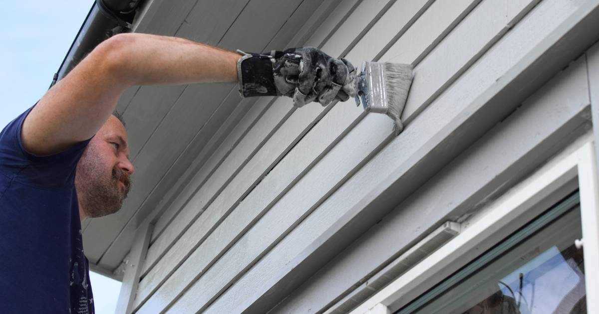 Detail view of paint being applied to horizontal house siding.